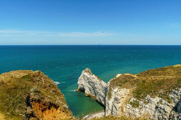 A cliff in the ocean with a rock resembling an elephant in the Etretat, Normandy, France The beach is visible below. And the calm blue water The water is blue, the sky is calm and transparent