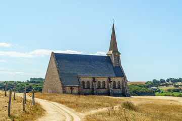A church in Etretat in France with a steeple is in a field. The church is old and has a weathered appearance. The sky is clear and the sun is shining brightly. Concept of peace and tranquility