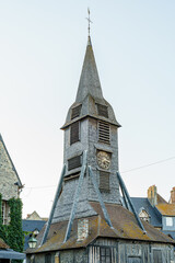 An ancient wooden chapel tower of Eglise sainte Catherine with a pointed tip. In France, in Normandy city Honfleur. There is a clock on the tower that shows 15 minutes past 9 It is evening time