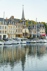 A row of boats are docked in a harbor, with a church in the background in city Honfleur in France Normandy The scene is peaceful and serene, with the boats reflecting the calm water