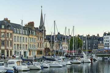 A row of boats are docked in a harbor, with a church in the background in city Honfleur in France Normandy The scene is peaceful and serene, with the boats reflecting the calm water