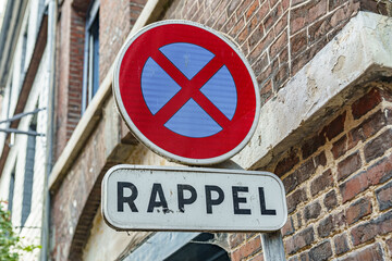 A red Round sign no stopping and white sign with a black letter RAPPEL on it in France. The sign is on a brick wall