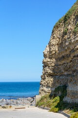 A rocky shoreline with a blue ocean in the background in Normandy France. The ocean is calm and the rocks are jagged