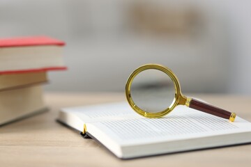 Magnifying glass and books on wooden table, closeup