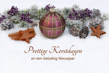 Kerstkaart met groeten in het Nederlands: Decoratie met kerstballen en dennentakken in de sneeuw. Prettige Kerstdagen en een Gelukkig Nieuwjaar. © Racamani