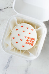 Birthday little cake with white cream cheese frosting decorated with red cream hearts on top. Trendy Korean bento cake as a gift for Valentine's Day in white box on the white marble background