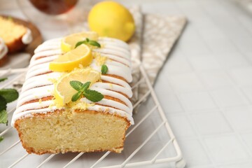 Delicious lemon cake with glaze, fresh fruit slices and mint on light tiled table, closeup. Space for text