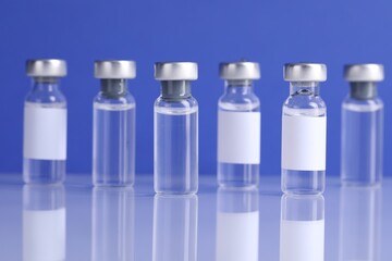 Vaccine in vials on light mirror surface against blue background, closeup