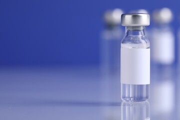 Vaccine in vial on light mirror surface against blurred blue background, closeup. Space for text