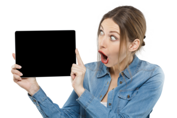 Surprised young woman in denim pointing at a blank black tablet screen, showing copy space