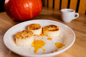 Minimalist food scene with golden cottage cheese pancakes topped with pumpkin sauce, pumpkin and coffee in background. Warm autumn light, cozy atmosphere, rustic wooden table
