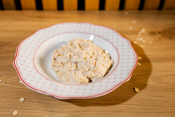 Creamy oatmeal served on a patterned plate over a wooden table, styled with scattered oat flakes for a warm, homemade look.