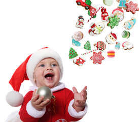 Cute little baby in Santa costume looking at flying Christmas treats on white background