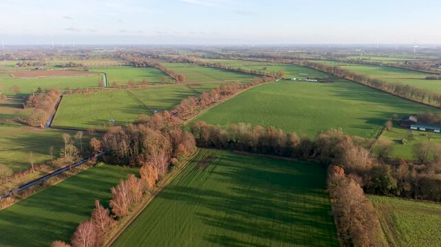 Aerial view of rural fields with crop rows, tree shadows, canal, and farm buildings sunlit landscape blending agriculture, infrastructure, and natural geometry.
