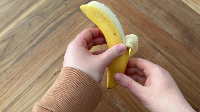 Female hand holding and peeling a banana on a wooden table. 