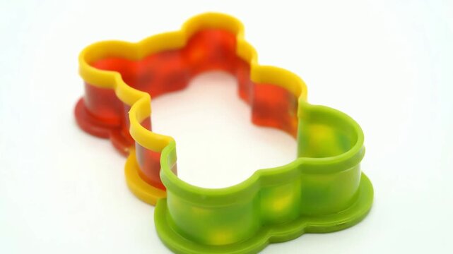 A vibrant multi colored plastic teddy bear cookie cutter isolated on a bright white background for baking fun