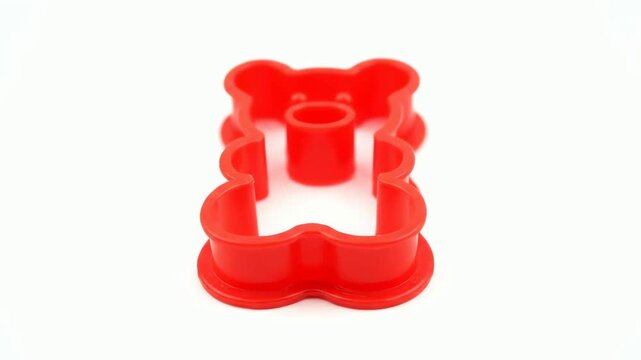 Vibrant red plastic cookie cutter in the shape of a cute teddy bear isolated on a white studio background.