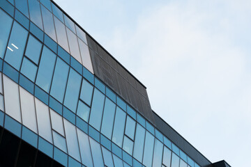 Contemporary office building with reflective blue glass windows and geometric design, photographed from a low angle. Suitable for illustrating architecture, business, or urban development concepts.