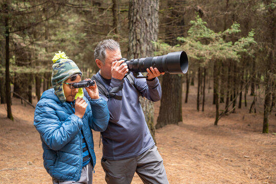 Grandfather and grandson enjoying nature, birdwatching, and photography hobby in forest