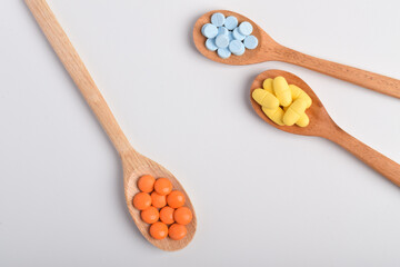 Various vitamin pills and tablets in wooden spoons on white background, top view. Concept of medication, supplement dosage and pharmaceutical products.