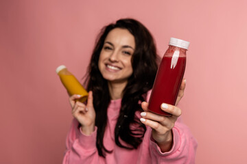 Contented cute young dark-haired female posing on the pink background with her favorite bottled soft drinks in both hands. Healthy beverage concept
