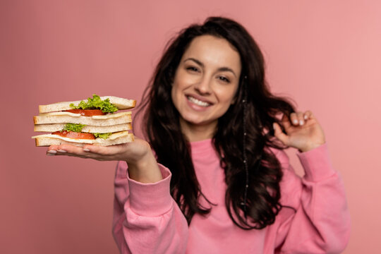 Cheerful young beautiful dark-haired woman demonstrating her favorite sarnies in front of the camera on the pink background. Healthy snack concept