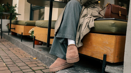 Woman wearing comfortable beige slippers and wide grey pants sitting at an outdoor cafe