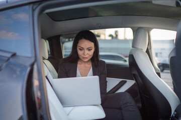 Beautiful businesswoman using laptop while sitting on back seat in the car while working online. Business, people, distance work concept © Vlad