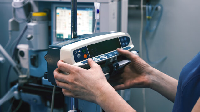 Medical professional adjusting a modern infusion pump in a clinical setting, showcasing advanced healthcare technology and patient care equipment in a sterile environment