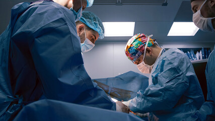Medical professionals in surgical attire are performing a complex operation in a sterile...
