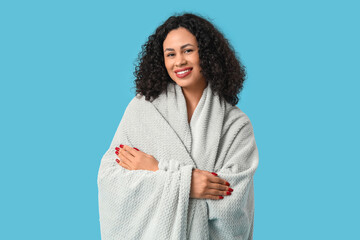 Beautiful young African-American woman with cozy blanket on blue background © Pixel-Shot