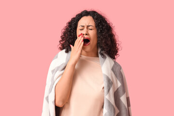 Beautiful young African-American woman with cozy blanket yawning on pink background © Pixel-Shot