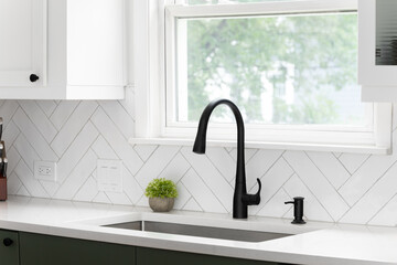 Sink detail shot in a luxury kitchen with white herringbone backsplash tiles. white marble...