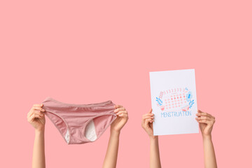 Female hands with period panties and calendar on pink background