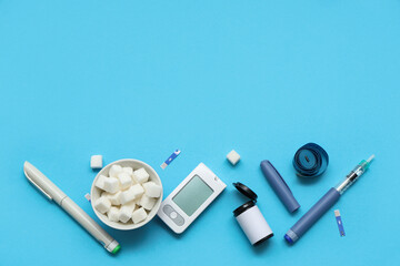 Digital glucometer, lancet pens,  test strips, measure tape and refined sugar cubes in bowl on blue background