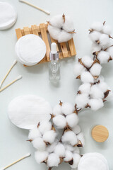 Composition with cosmetic products, beautiful cotton branch, pads and swabs on light background
