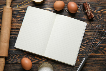 Composition with blank recipe notebook, eggs and rolling pin on black wooden background
