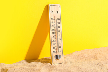Weather thermometer on sand against yellow background
