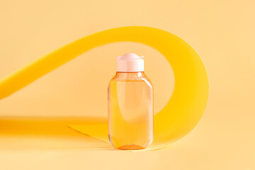 Bottle of micellar water and folded paper sheet on pale yellow background