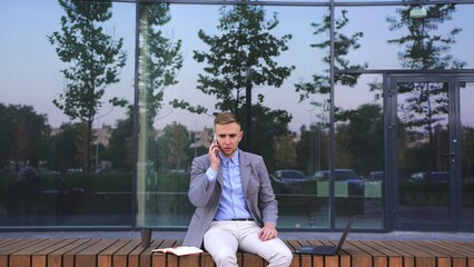 Fototapeta premium Shocked young man answering the call, sitting on the bench outdoor. Slow motion