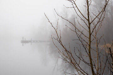 Fisherman on pier on foggy lake