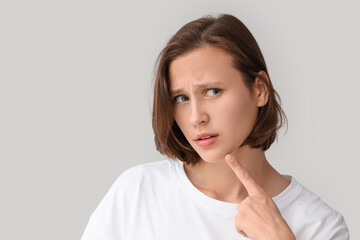 Fototapeta premium Beautiful young woman with acne problem pointing at her skin on grey background