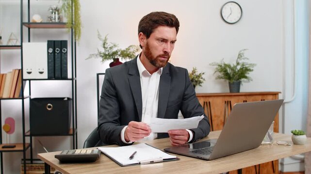 Middle-aged businessman at home office enters numbers on laptop checks amounts with calculator and receipts. Freelancer guy at table reviews bills and signs documents with calm focus and steady hand.