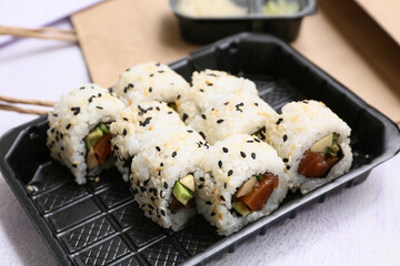 Plastic plate with tasty sushi roll on lilac grunge background, closeup. Delivery concept