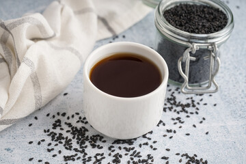Cup of oil and jar with sesame seeds on white grunge background