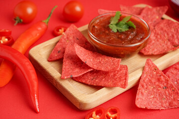 Wooden tray with red nachos, salsa sauce and chilli on color background