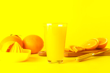 Glass of fresh orange juice and juicer on yellow background