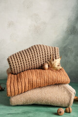 Autumn composition with stack of stylish sweaters, foliage and acorns on green background