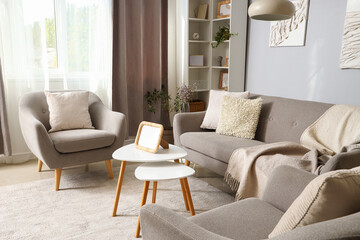 Interior of modern living room with grey sofa, armchairs and blank photo frame on coffee table