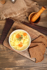 Bowl of tasty chicken soup and bread on wooden background